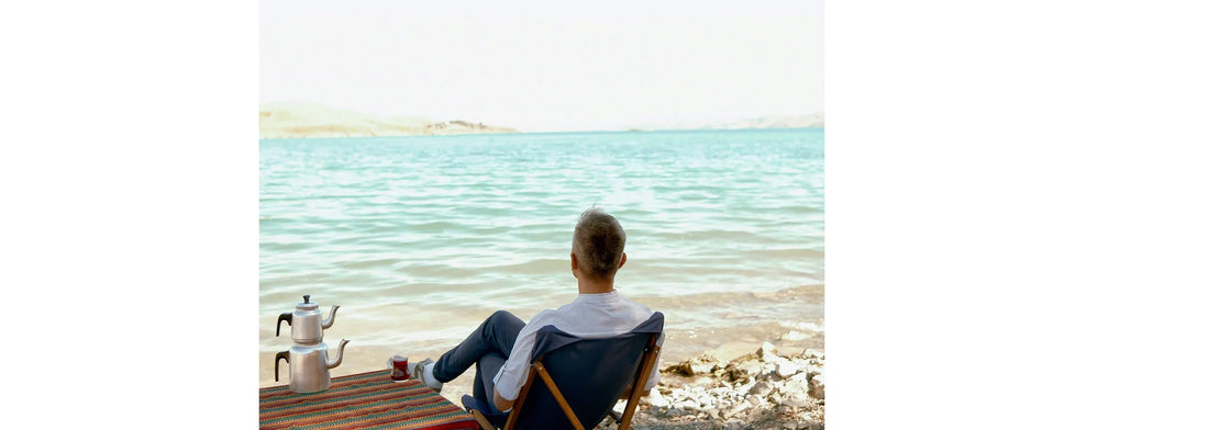 Person sitting on a chair by the water, looking out at the sea. for YASOU's blog post called Beyond the Surface: Decoding ‘The Greek Way’ of Cellular Health.
