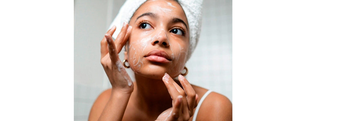 Brown woman with bathroom towel wrapped around her hair cleansing her face. A photo for YASOU's blog post called "The Double Cleansing Method For Glowing Skin"