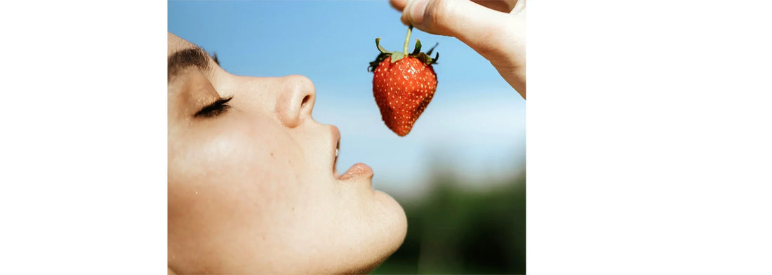 Vitamin C: Just a Trend or the Key to Ageless Skin? blog post photo of woman's face upclose getting ready to put a strawberry into her mouth.