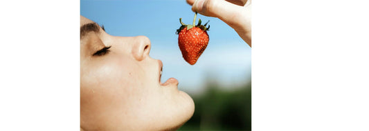 Vitamin C: Just a Trend or the Key to Ageless Skin? blog post photo of woman's face upclose getting ready to put a strawberry into her mouth.