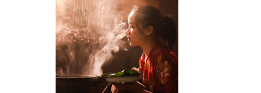 Person near a steaming pot, steaming her face. For blog post called "What are the real skin benefits of steaming your face?"