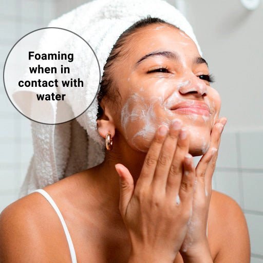 Woman applying foaming cleanser to her face with a towel on her head, text 'Foaming when in contact with water'.